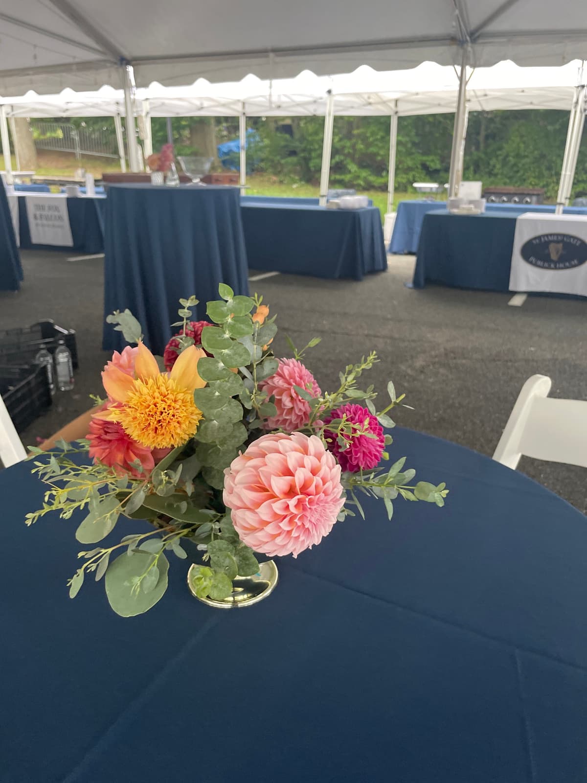 A lush floral centerpiece on a navy blue tablecloth featuring a large blush pink dahlia, a magenta dahlia, and a yellow dahlia accented with eucalyptus greenery.